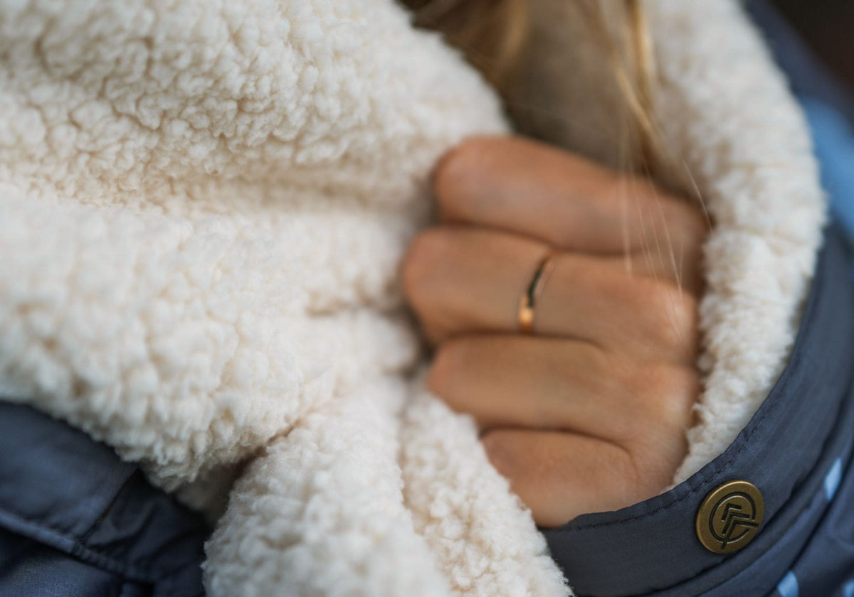 Nahaufnahme einer Hand, die das cremefarbene Sherpa-Fleece einer VOITED Cloudtouch Decke hält.